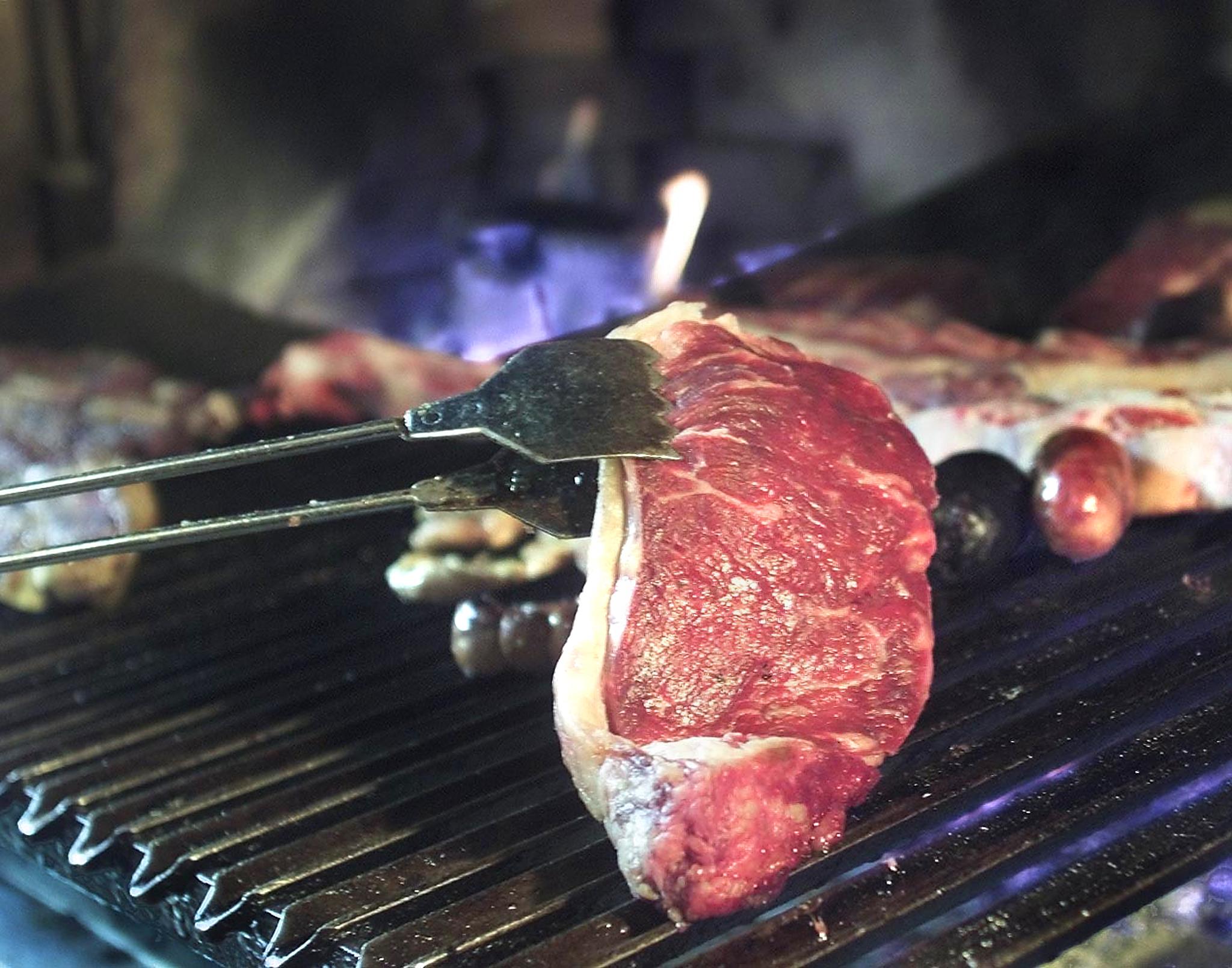 A beef steak is put on the grill of a barbecue restaurant. The World Health Organization said cooking red meat at high temperatures (as in barbecuing or pan-frying) produces certain types of carcinogenic chemicals, and they classified its consumption in the same category as tobacco.